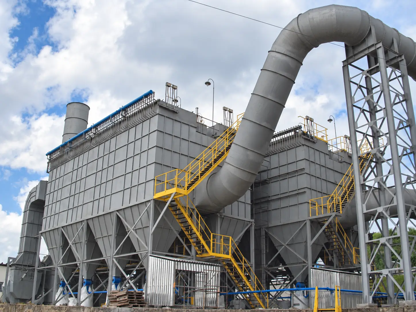 Gray baghouse assembly with hoppers, yellow ladders, and a large duct