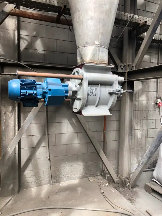 Rotary airlock installed beneath a hopper, with blue gearmotor and metal casing