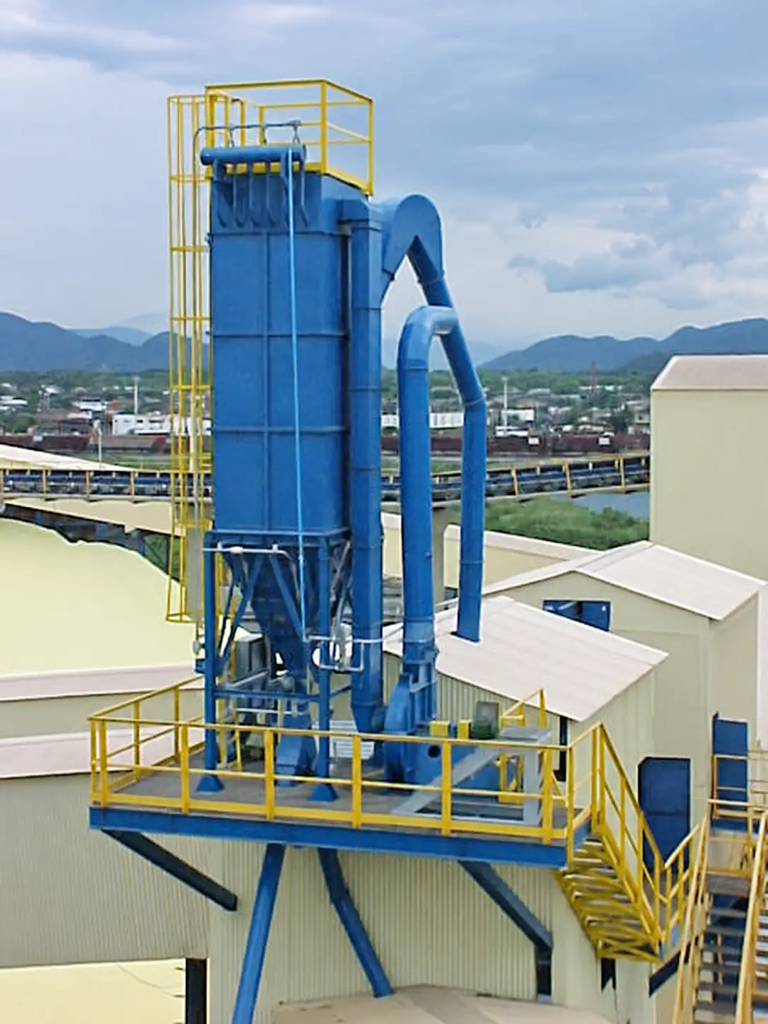 Blue baghouse on an elevated platform, with ductwork and yellow access structures
