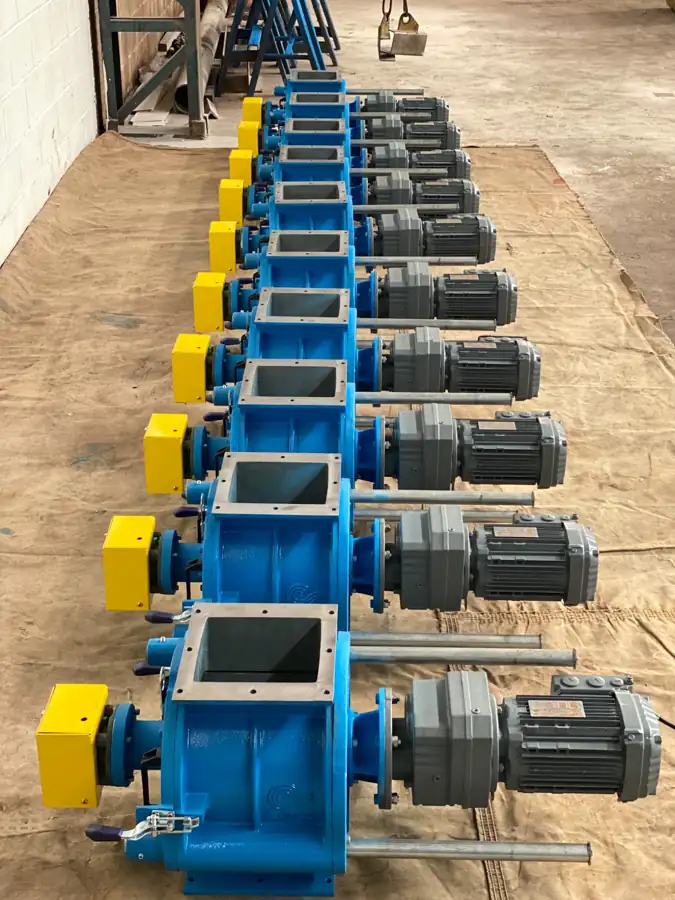 Batch of blue rotary airlocks with gearmotors and yellow guards, lined up at the factory